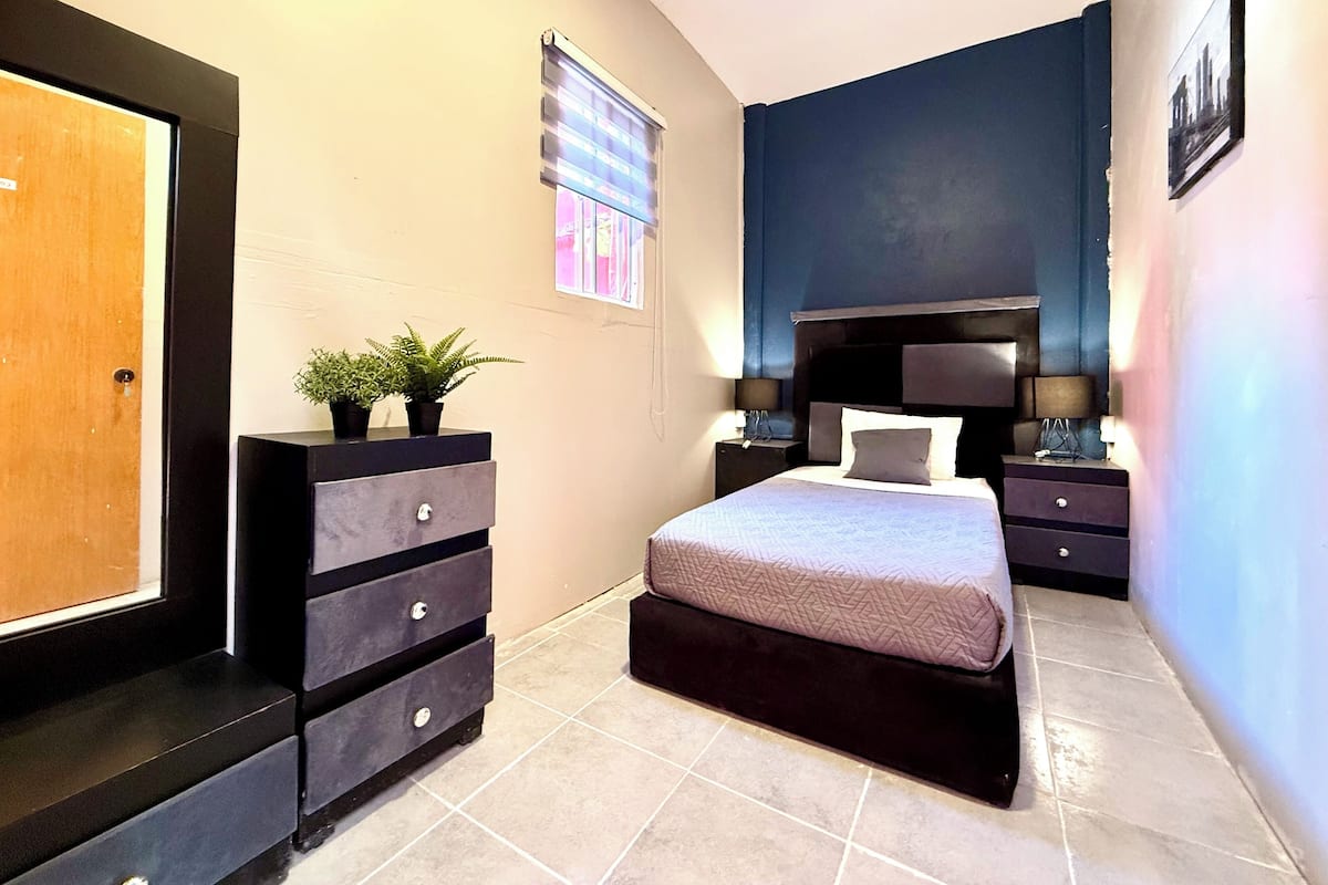 A bedroom with a bed, a dresser, a nightstand, and a window with blinds.