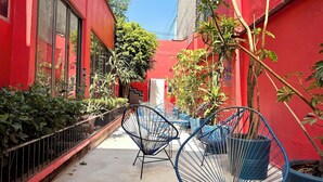 A narrow alley with red walls, potted plants, and blue wire chairs. - RMS Hostal - Roma Norte (Mexico City)