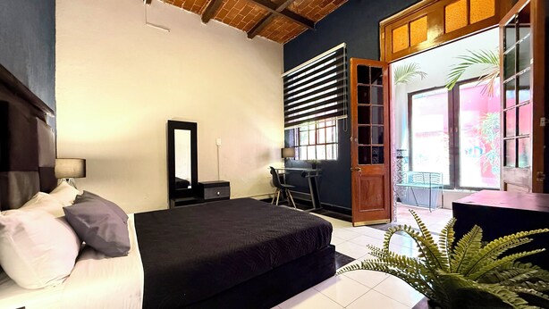 A bedroom with a bed, a desk, a chair, a mirror, and a door leading to a balcony with plants. - RMS Hostal - Roma Norte (Mexico City)