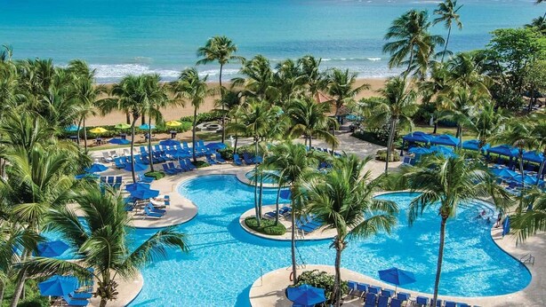 A resort with a large pool surrounded by palm trees and beach views. - Ocean & Mountain Views and Exclusive Beach Access in a Tropical Studio Suite (Rio Grande)