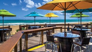 A beachside restaurant with outdoor seating, a wooden deck, and a signpost listing various cities. - Ocean & Mountain Views and Exclusive Beach Access in a Tropical Studio Suite (Rio Grande)