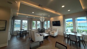Un amplio hall de hotel con diseño moderno, que incluye un candelabro, asientos cómodos, un televisor de pantalla plana y ventanas grandes con vistas al exterior.