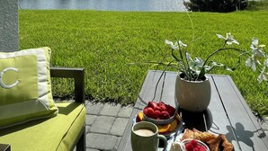 Una mesa con una taza, un plato de fruta y un pastel, frente a una vista del lago y árboles.