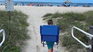 Un sendero que conduce a una playa con gente y sombrillas.