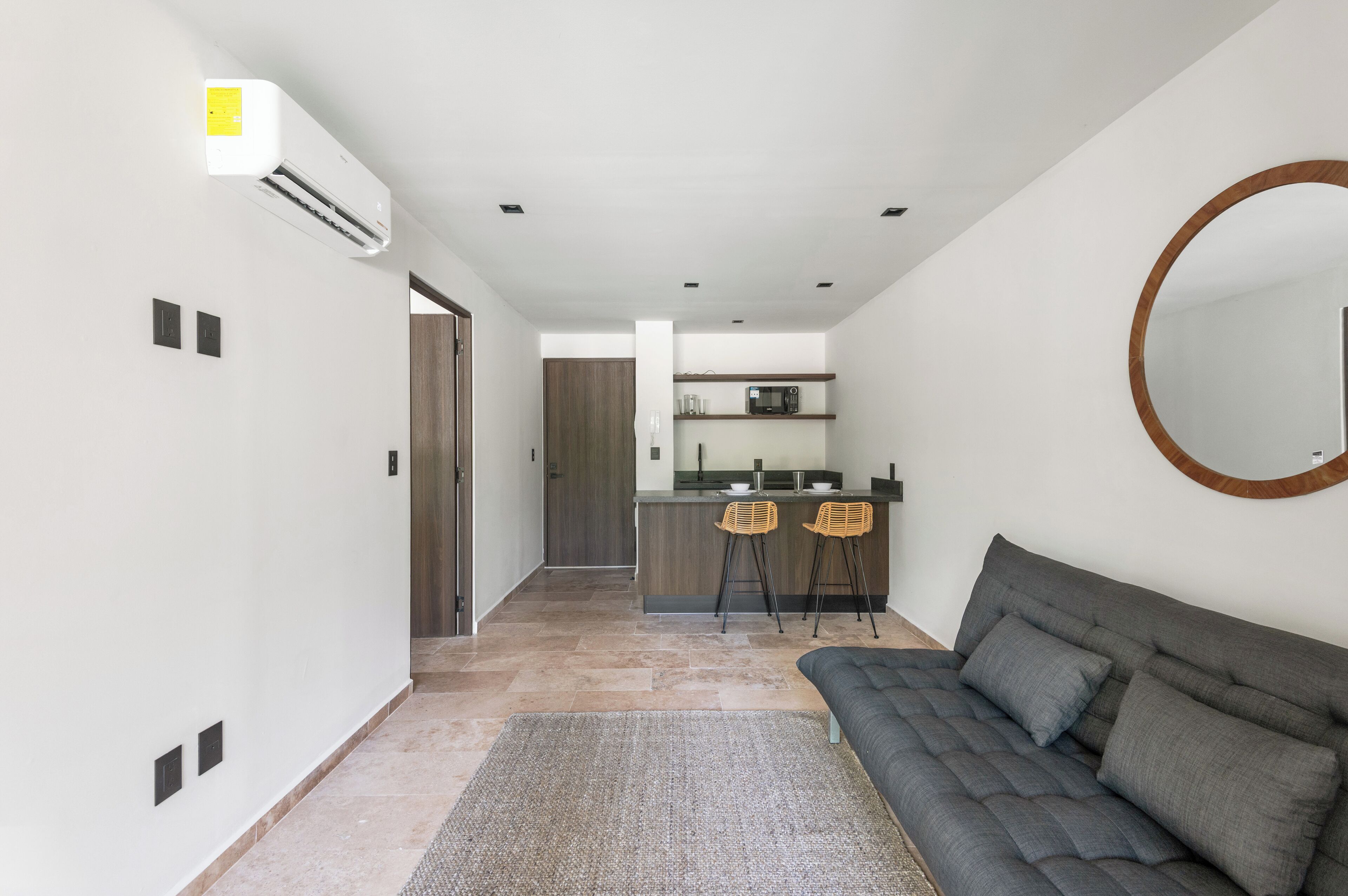 Un espacio moderno para vivir con cocina, sofá y un espejo redondo.
