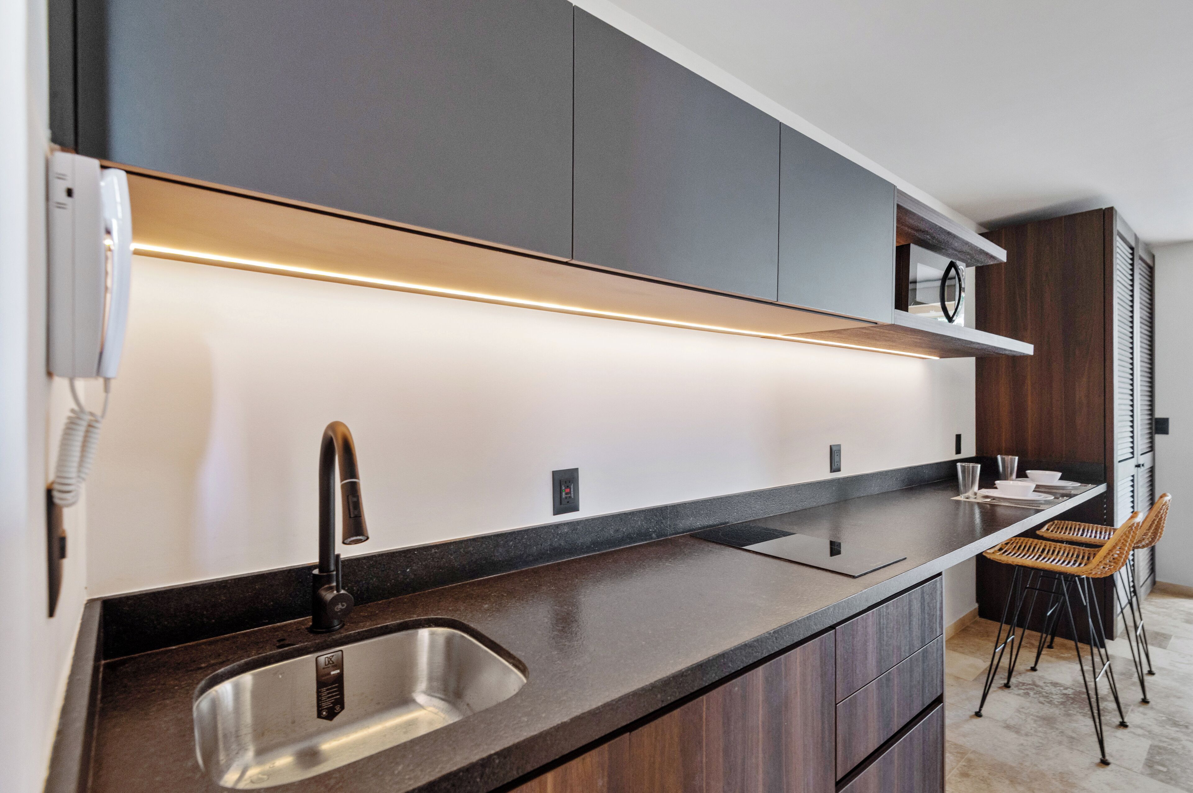 A modern kitchen with a stainless steel sink, dark wooden cabinets, and a built-in light strip above the countertop.