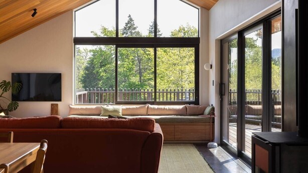 A modern living room with a large window, a built-in bench, a TV, and a fireplace. - Redwood Cosy Hanmer Springs (Hanmer Springs)