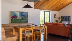 A modern living space with a wooden dining table, orange sofa, and a large painting on the wall. - Redwood Cosy Hanmer Springs (Hanmer Springs)