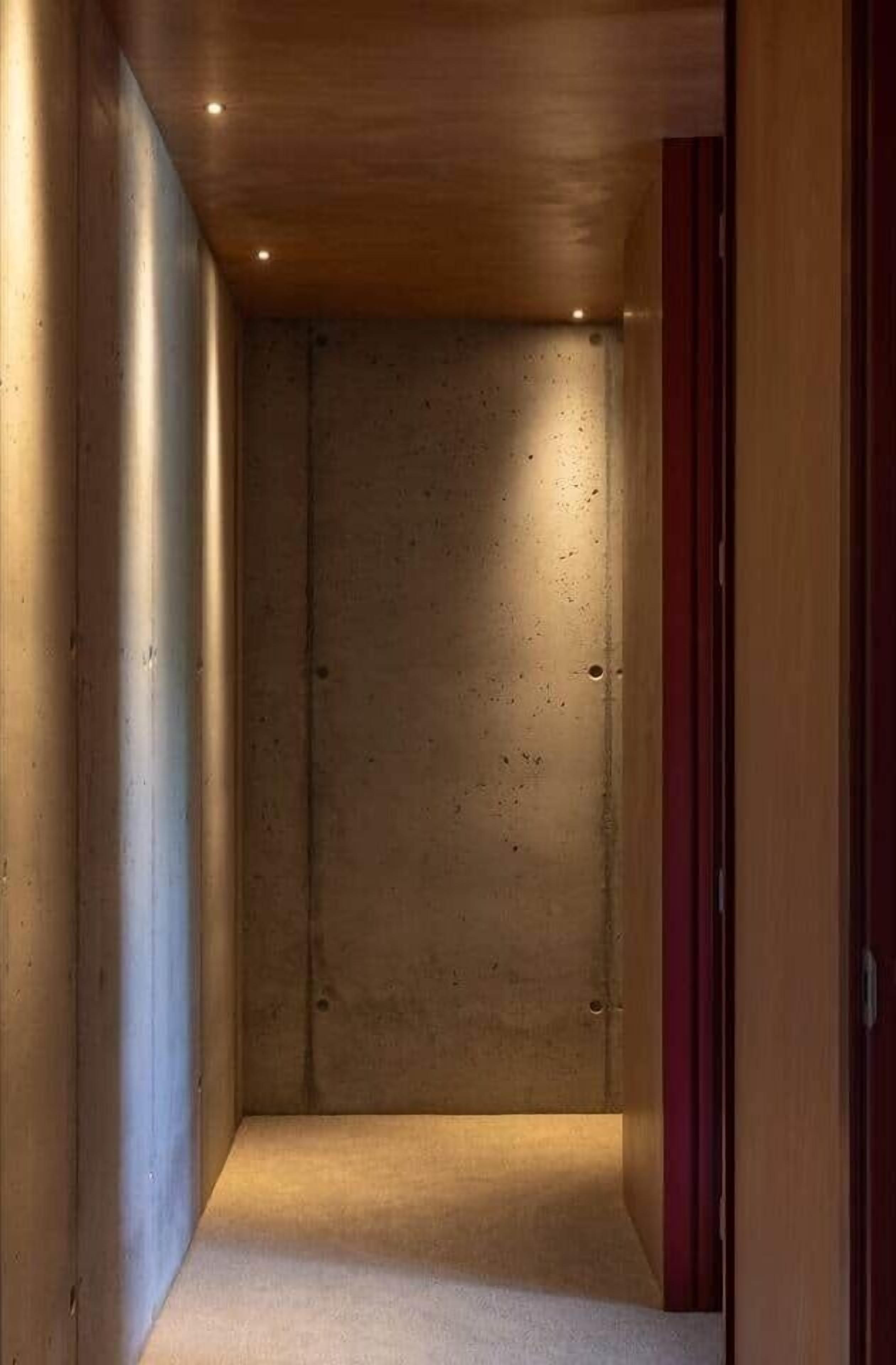 A narrow hallway with a concrete wall and a wooden ceiling.