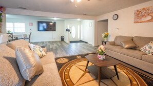 A spacious living room with a large flat-screen TV, a ceiling fan, and a dining area in the background. - 8 Min ATandT Stadium | Central 4BR Retreat (Grand Prairie)