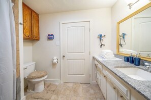 Une salle de bain comprenant des toilettes, un bidet et un lavabo. On y trouve un porte-serviettes avec des serviettes, un miroir et une trousse de premiers secours accrochée au mur.
