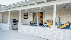 A covered patio with white brick walls and a pergola. There are outdoor seating areas with blue chairs and cushions. - 8 Min ATandT Stadium | Central 4BR Retreat (Grand Prairie)