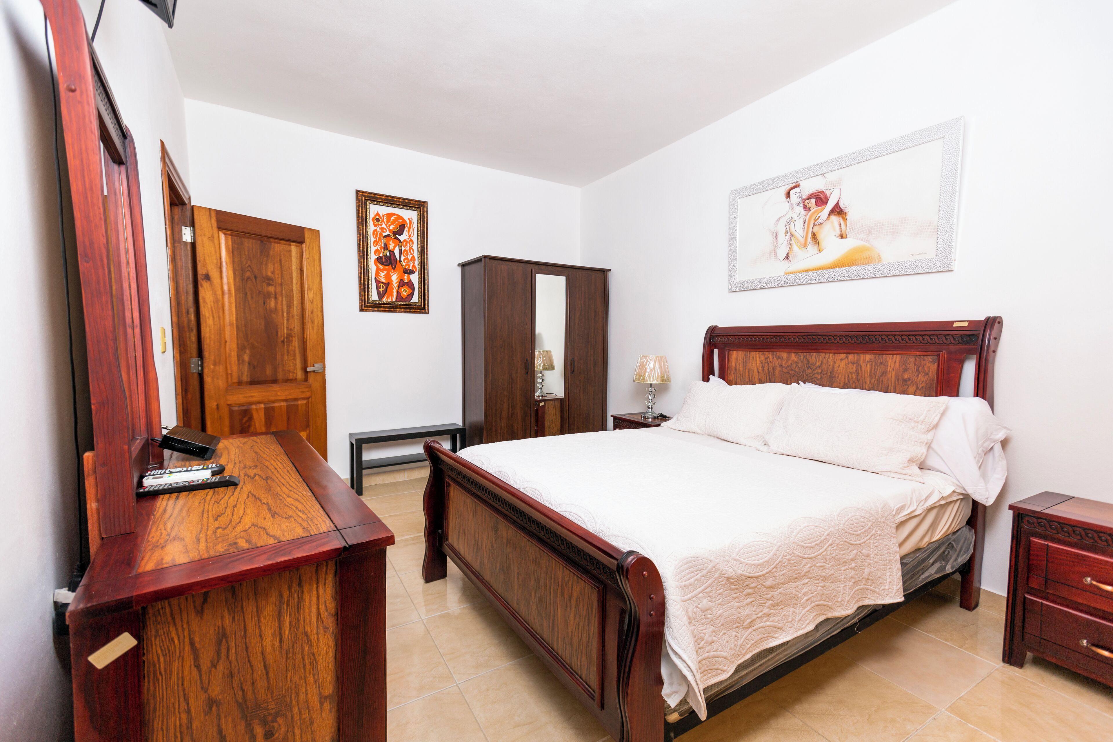 Une chambre à coucher avec un lit en bois, une commode en bois, un miroir et un tableau encadré accroché au mur.