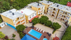 Un hotel de varios pisos con zona de piscina en la azotea, que incluye sillones de descanso y una piscina más pequeña.