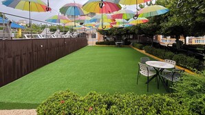 Un patio con césped artificial, mobiliario exterior y sombrillas de colores.