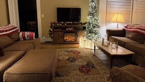 A cozy living room with a fireplace, a Christmas tree, and a television. - Cozy Ludlow, Vermont Farmhouse Ski Retreat with hot tub and fire pit (Ludlow)