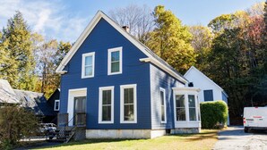 A two-story house with a blue exterior, a front porch, and a garage. - Cozy Ludlow, Vermont Farmhouse Ski Retreat with hot tub and fire pit (Ludlow)