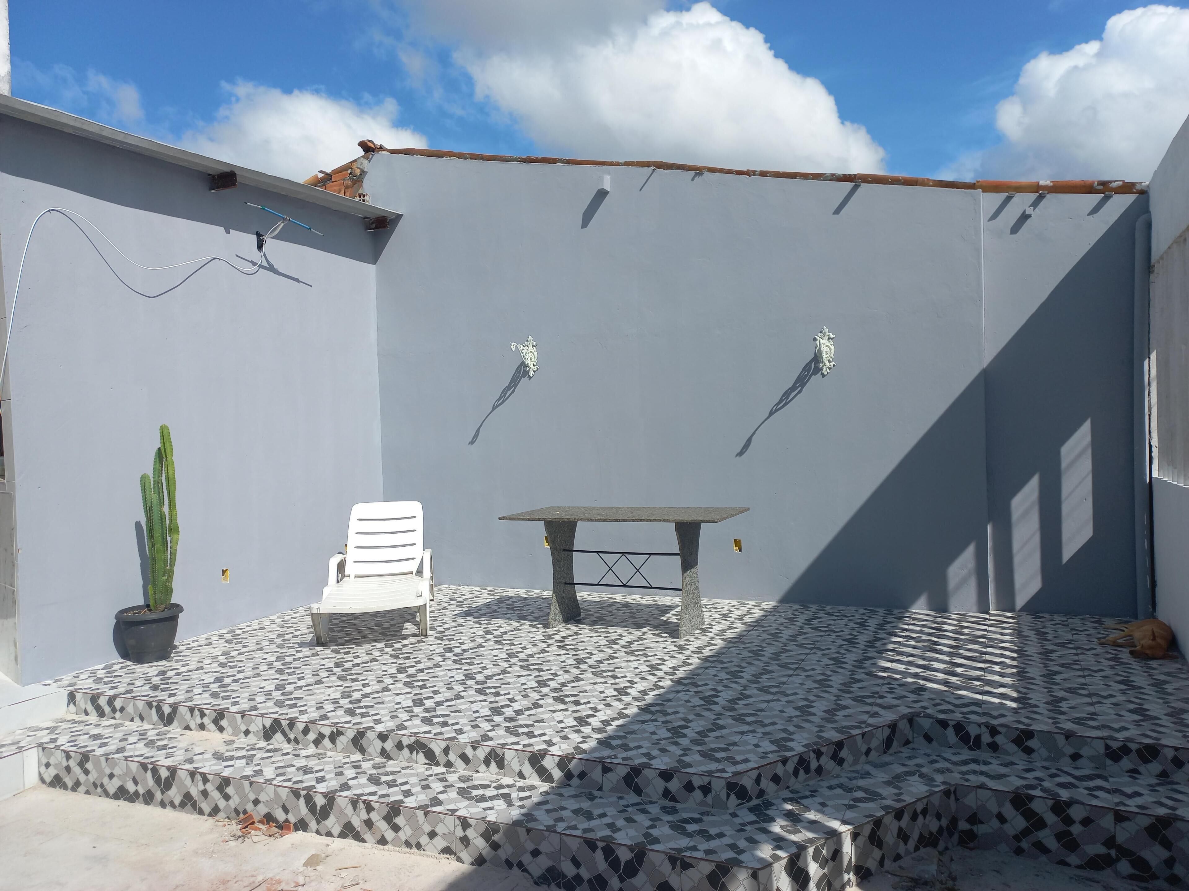 A patio with a tiled floor, a white chair, a table, and a potted plant.