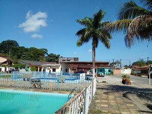 Une piscine entourée d’une clôture bleue, bordée de bâtiments résidentiels et agrémentée d’un palmier.