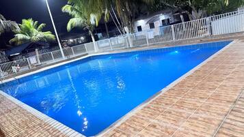 Una piscina rectangular con borde de azulejos, rodeada por una valla blanca y palmeras.
