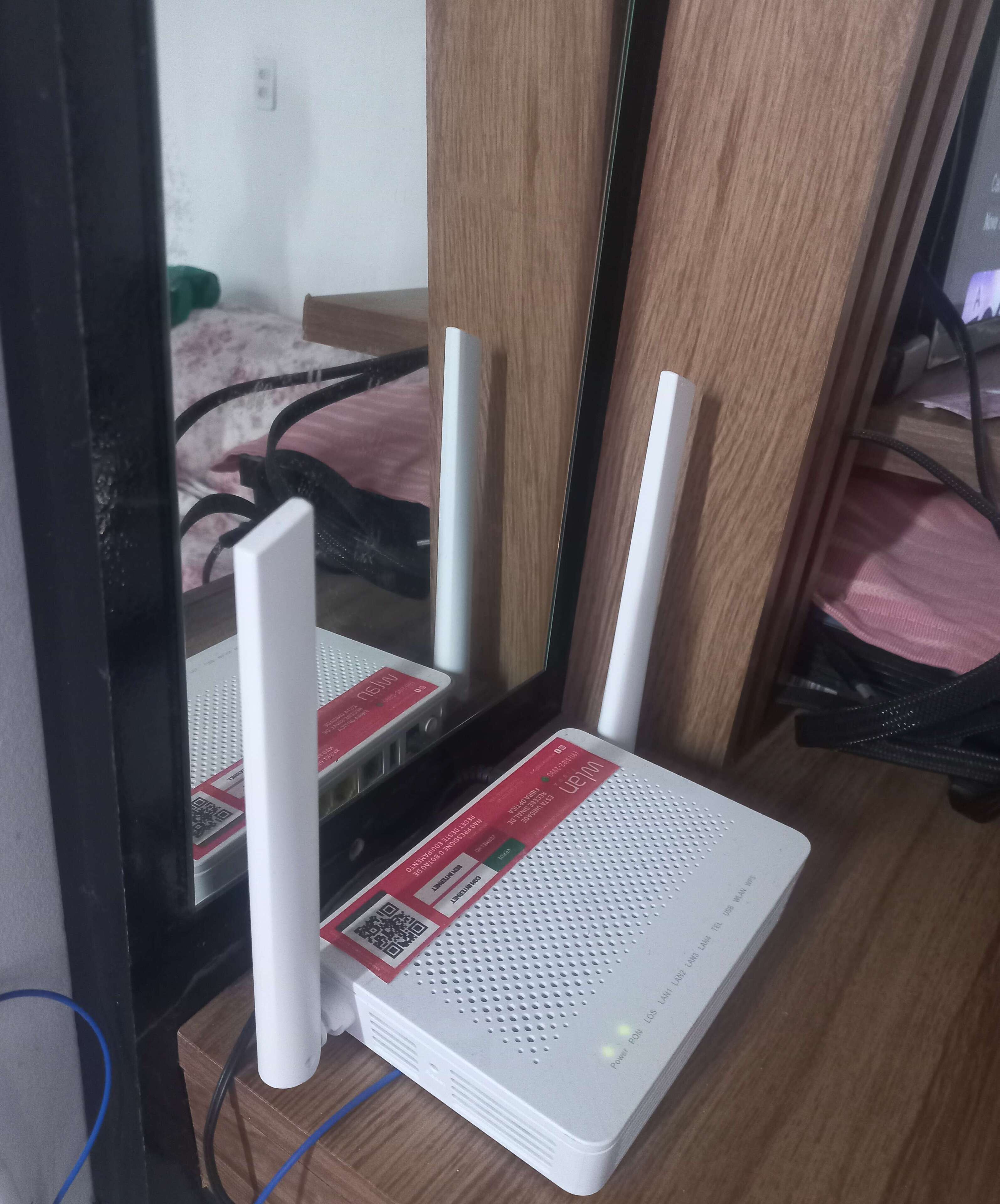 A white router with a red label on a wooden surface, connected to a black cable.