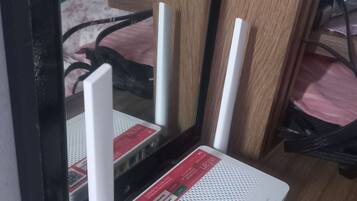 A white router with a red label on a wooden surface, connected to a black cable.