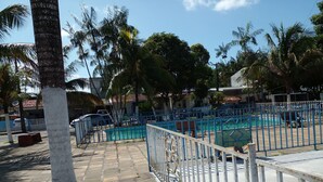 Ett inhägnat utomhusområde med en swimmingpool, palmer och en klarblå himmel.