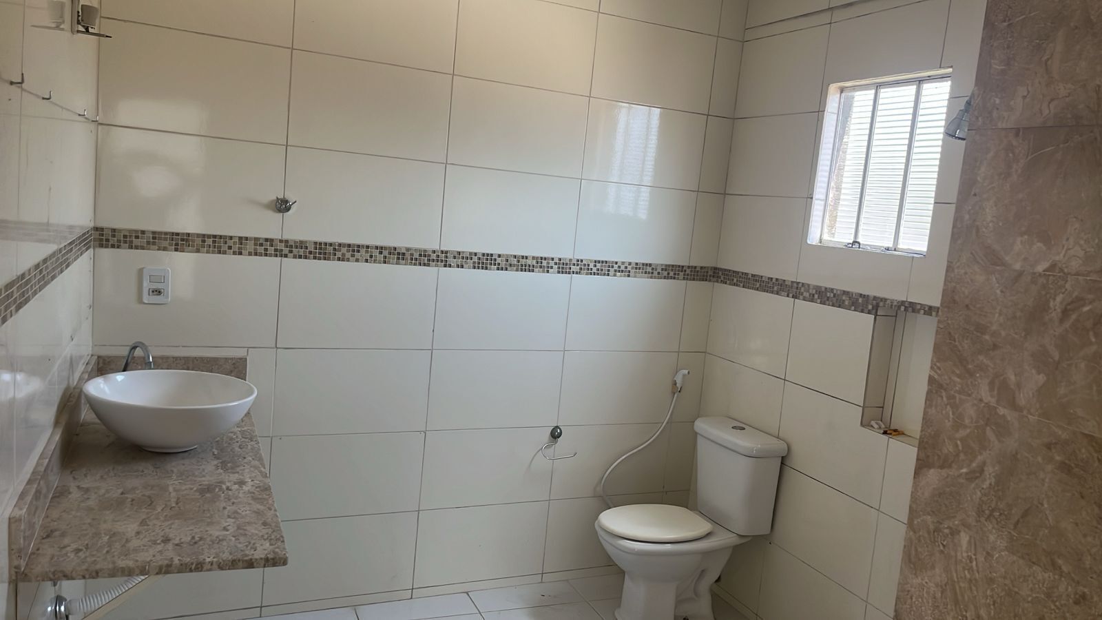 Un baño con lavamanos blanco, inodoro y una ventana pequeña.
