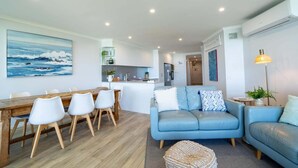 A modern living room with a blue sofa, a dining table with chairs, and a kitchen area in the background. - Breathtaking View! (Point Lookout)