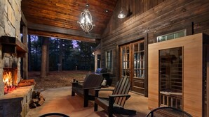 A wooden cabin with a stone fireplace, outdoor seating, and a large window. - Hot tub Sauna King • Fireplace • Pet‑Friendly (Broken Bow)