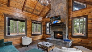 A log cabin interior with a stone fireplace, wooden walls, and large windows. - Hot tub Sauna King • Fireplace • Pet‑Friendly (Broken Bow)