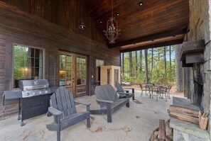 Un espace extérieur abrité comprenant un barbecue, des fauteuils Adirondack et une cheminée en pierre.