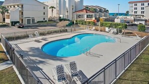 En swimmingpool med liggestole og et afspærret område, omgivet af bygninger og en klar himmel.