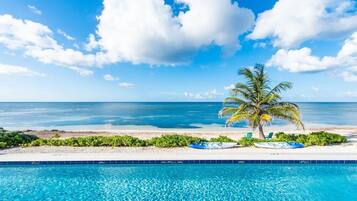 A poolside view with a clear blue sky, a palm tree, and a beach in the background.
