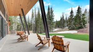 Une terrasse extérieure avec des chaises en bois et un barbecue, donnant sur une zone boisée.
