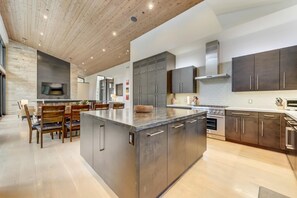 A modern kitchen with a large island, dark cabinetry, and a stone backsplash. - KBM Resorts | Walk to Slopes, Sports Court, Private Home Theater, Sleeps 16, Private Hot Tub PCO-184G (Park City)