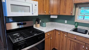 Una cocina compacta con armarios de madera, un horno de acero inoxidable, un microondas y un lavamanos.