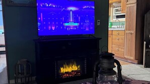 Una sala de estar con una televisión sobre un mueble bajo, una chimenea y una mesa redonda con un tapete decorativo.