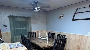 Un comedor con una mesa y sillas de madera, un ventilador de techo y una ventana con cortina.