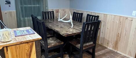 Un comedor con una mesa y sillas de madera, un ventilador de techo y una ventana con cortina.