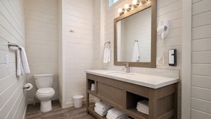 A bathroom with a wooden vanity, a toilet, and a mirror with lights.