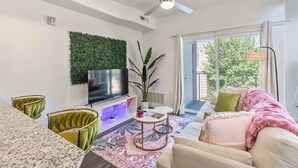 A modern living room with a flat-screen TV, green upholstered chairs, a white sofa, and a large window with a view of greenery. - NEW-KING Bed Loft Apartment / Downtown/ Free Garage Parking/ GYM (Salt Lake City)