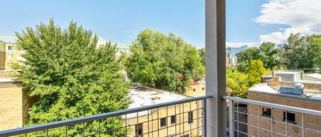 A view from a balcony overlooking a brick building with a visible sign, surrounded by trees and other buildings.