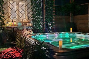 A hot tub with a wooden deck, surrounded by lush greenery and a decorative wall. - Estate for 27 people with SPA and Festive BARN (Sainte-Ursule)