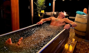A person relaxing in a hot tub with a wooden barrel and candles in the background. - Estate for 27 people with SPA and Festive BARN (Sainte-Ursule)