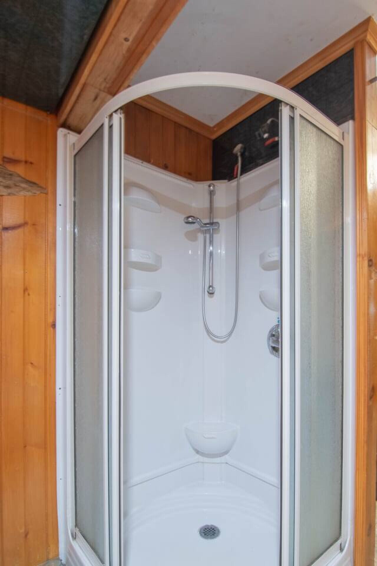 A corner shower stall with a glass door, a handheld showerhead, and a built-in seat.