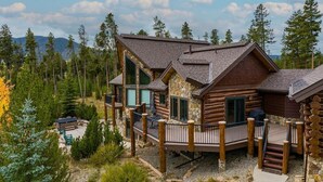 A log cabin with a deck, surrounded by trees and a mountain in the background. - Tabernash 5BR Retreat | Hot Tub, Golf & Skiing (Winter Park)