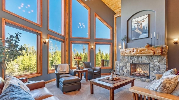 A spacious living room with large windows, a stone fireplace, and a cozy seating area. - Tabernash 5BR Retreat | Hot Tub, Golf & Skiing (Winter Park)