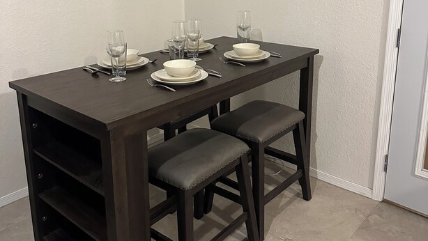 A dining area with a dark wooden table, two chairs, and a white air conditioning unit mounted on the wall. - Southwest-Chic 1BR Casita, Private Yard + Driveway, Northern Phoenix Getaway (Glendale)