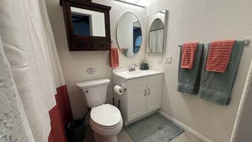 A bathroom with a toilet, sink, mirrors, and towels.